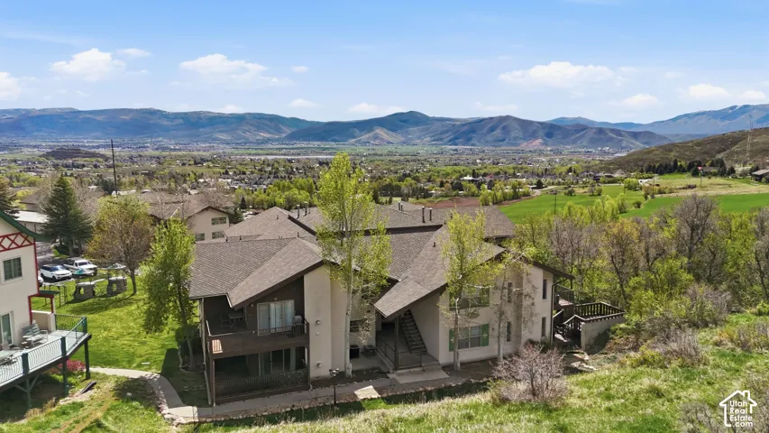 Multi-level structure with multiple balconies and a sloped roofline, set against a backdrop of distant mountains and a valley