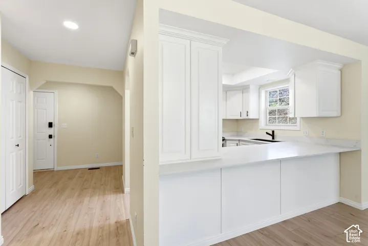 Wood-finish flooring, recessed lighting, white shaker-style cabinetry, and light-colored countertops