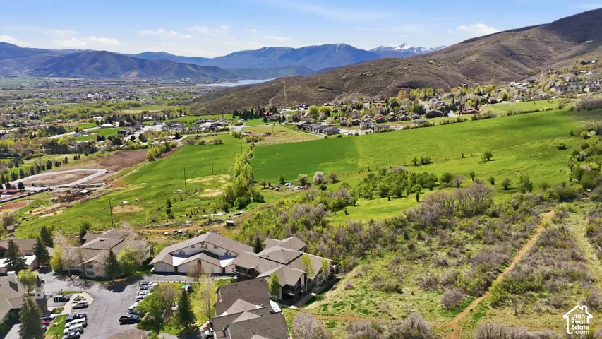 Expansive mountain landscape with a distant body of water, bordered by green fields and residential structures