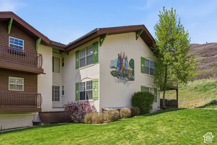Exterior featuring stucco and wood siding, green decorative shutters, and a balcony with an ornate railing