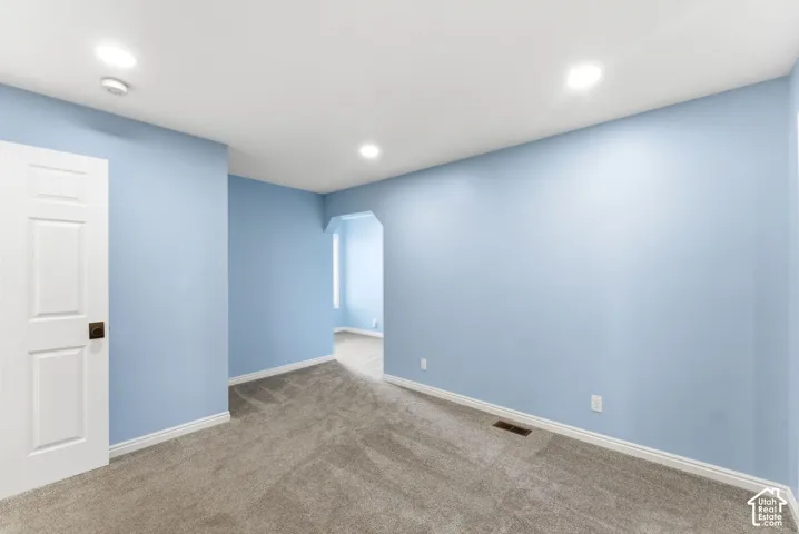 Recessed ceiling lighting, paneled interior door, dark bronze hardware, arched entryway, and gray carpet flooring