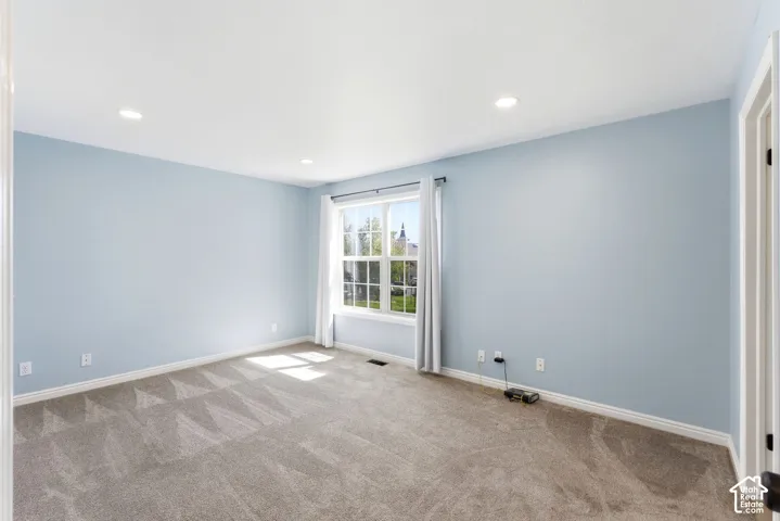 Recessed ceiling lighting, light blue wall paint, window with white trim, gray patterned carpet, and white door trim