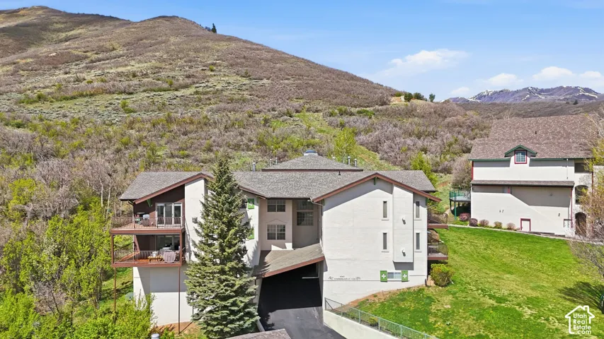 Multi-level building with individual balconies, covered entryway, and a sloped grass terrain