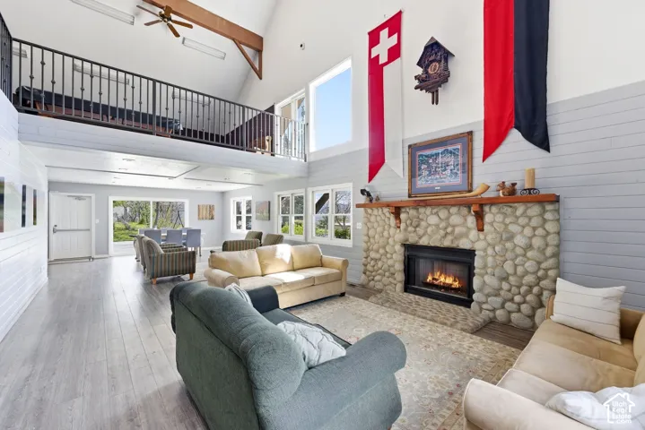 Spacious great room featuring vaulted ceilings, wood-finish flooring, an exposed beam, a stone-faced fireplace, and an upper-level balcony with a wrought iron railing
