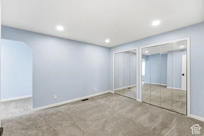 Recessed ceiling lighting, two sets of mirrored bi-fold closet doors, light blue wall finishes, white trim, and gray carpeting