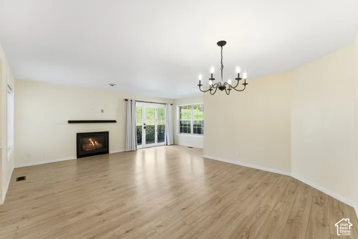 Wood-finish flooring, built-in fireplace with mantel, French doors, multiple windows, and a chandelier