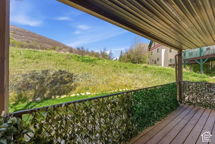 Covered outdoor deck with wood-finish flooring, featuring a slatted privacy screen and a metal railing
