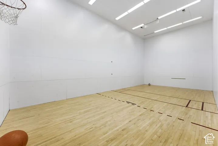 Indoor court featuring wood-finish flooring with court markings, bright white walls, and overhead fluorescent lighting