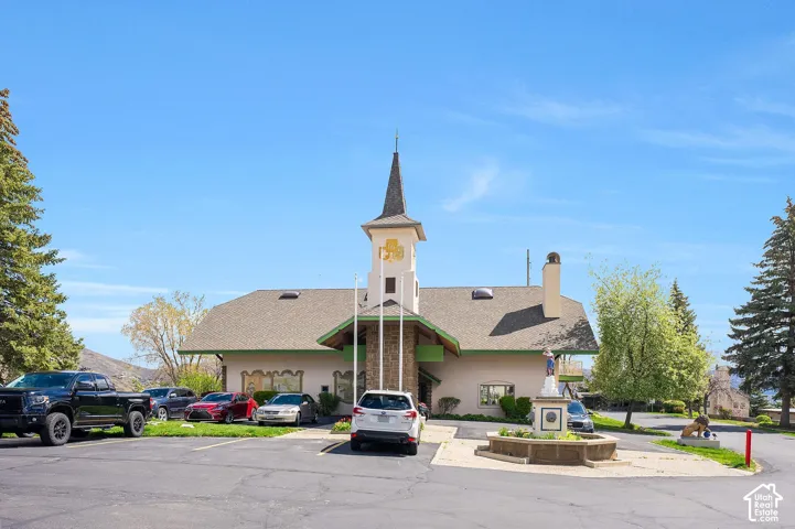 Building with distinctive spire, stone facade accents, pitched roof, and a circular planter with a central statue