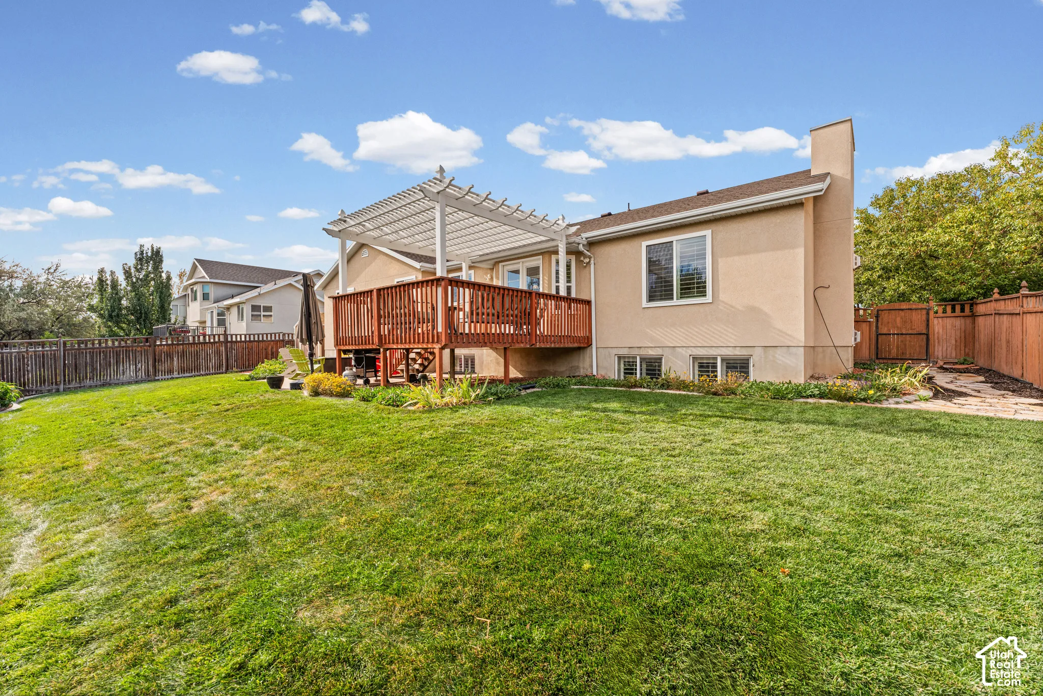 Expansive backyard featuring a manicured lawn, a two-story wood deck with a pergola, and a stone patio