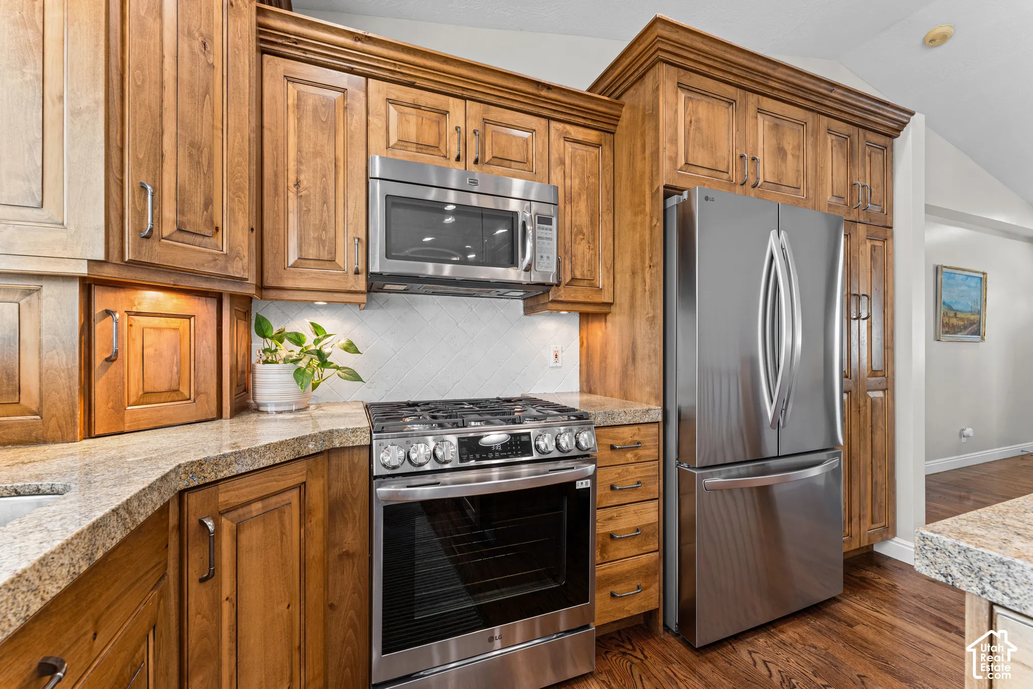 Kitchen featuring wood cabinetry, stainless steel appliances, speckled countertops, and a white tile backsplash