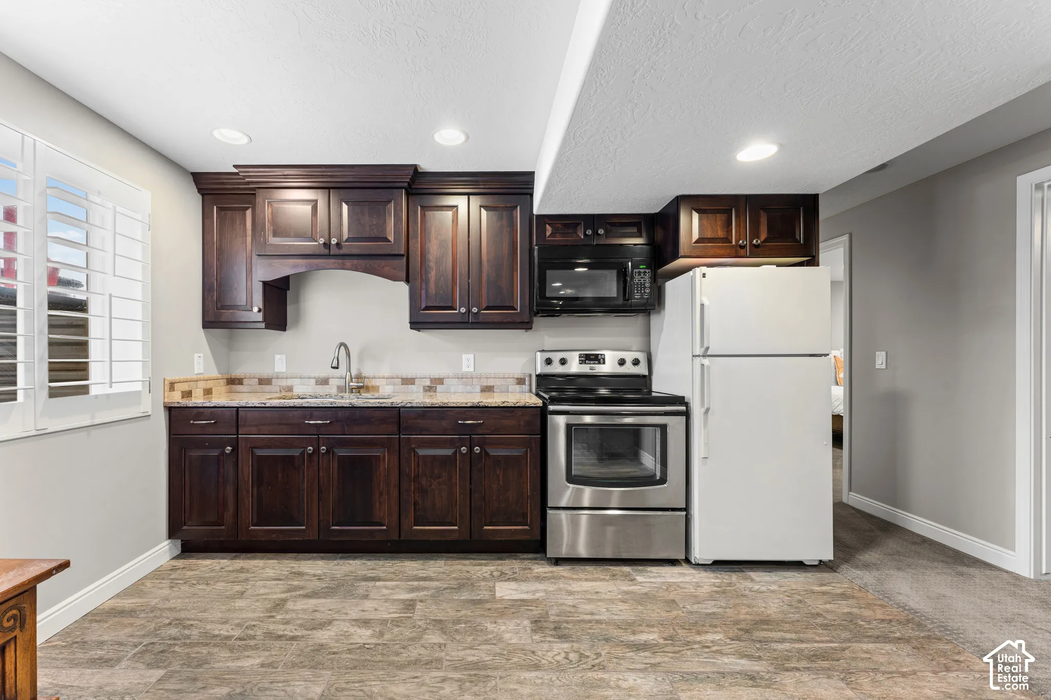 Kitchenette featuring dark wood cabinetry, stainless steel appliances, granite-look countertops, and a mosaic tile backsplash