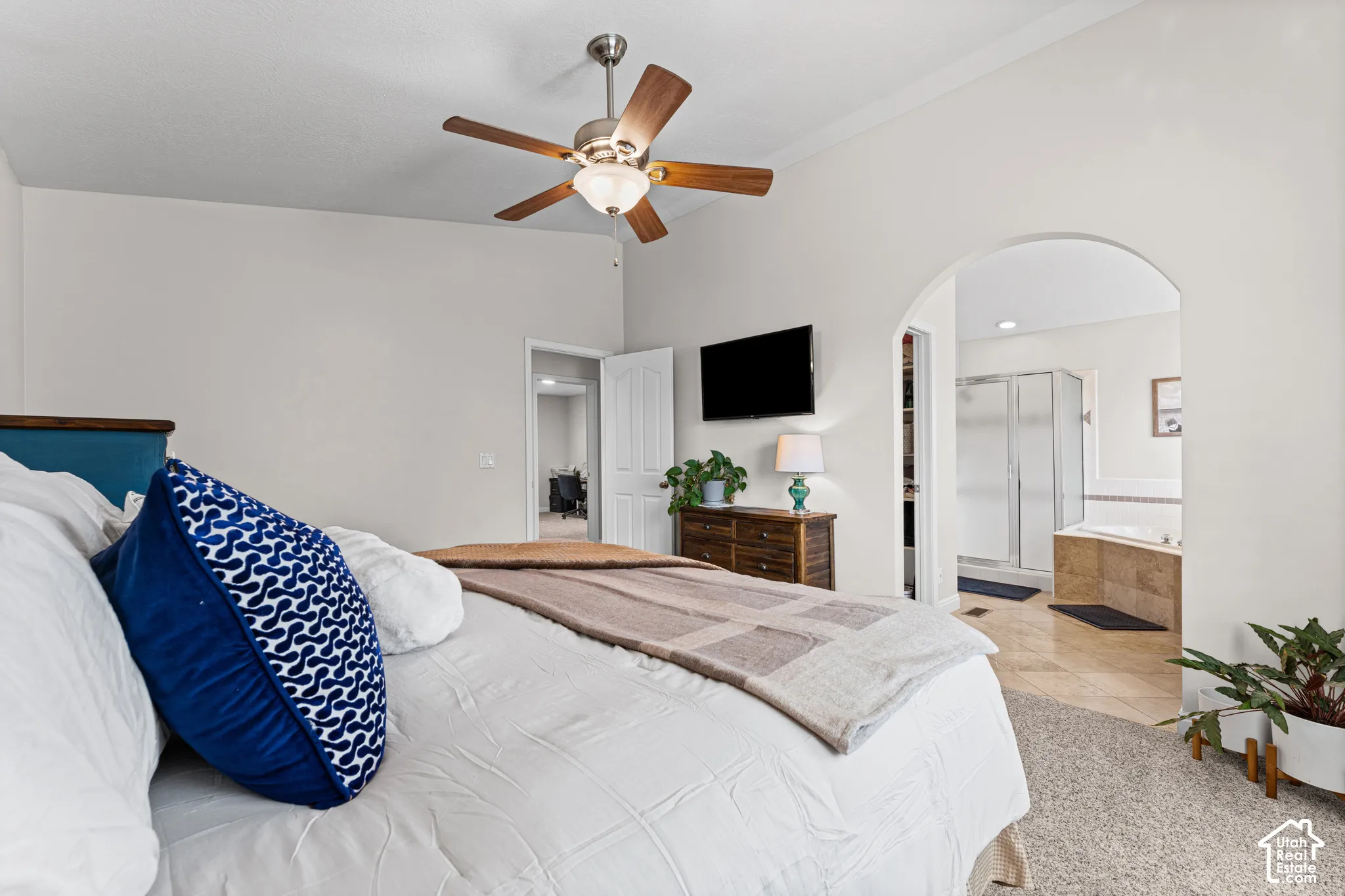 Ceiling fan with wood-finish blades, arched doorway, tiled bathroom flooring, built-in bathtub, and a glass-enclosed shower