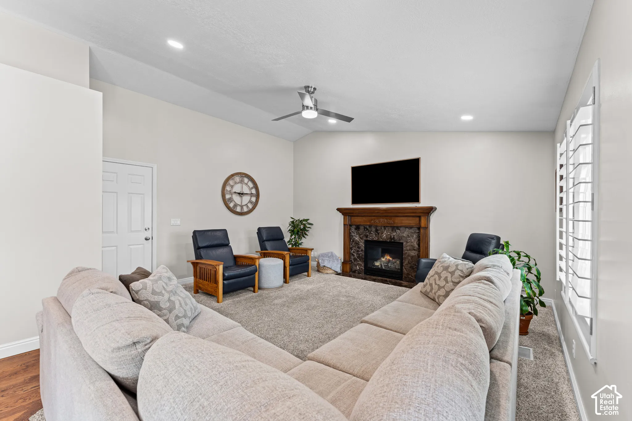 Spacious living area featuring a fireplace with a wood-finish mantel and stone surround, plantation shutters, recessed lighting, and a ceiling fan