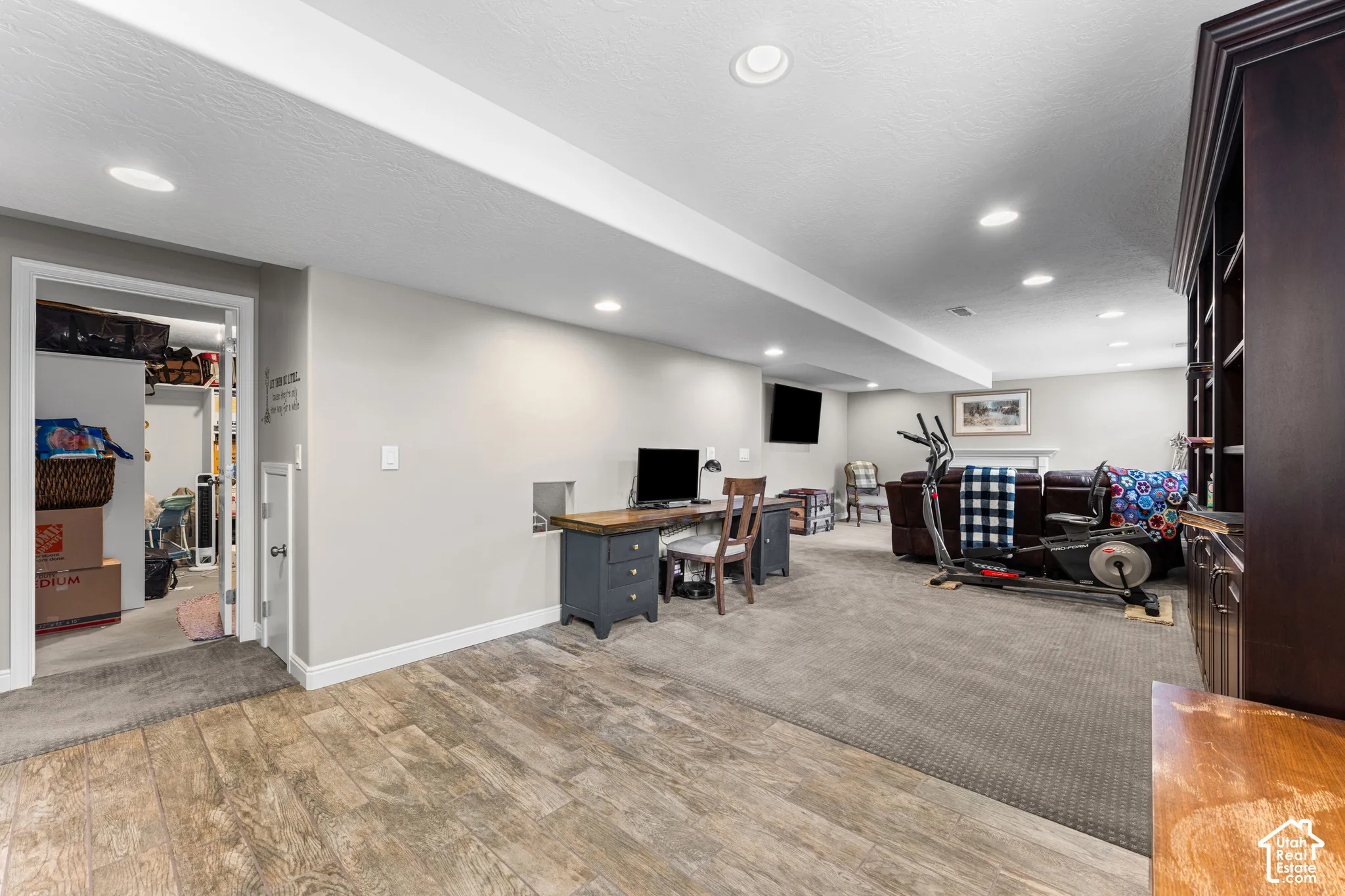 Recessed lighting illuminates the space, featuring wood-finish flooring transitioning to carpet, a built-in shelving unit, and a doorway accessing additional space