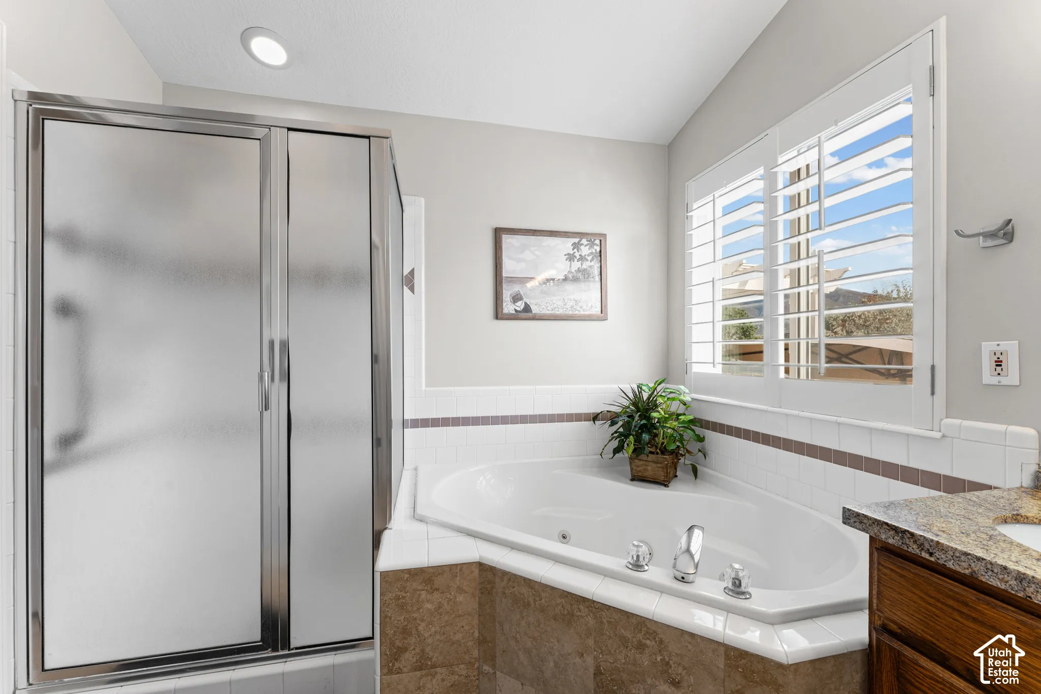 Frosted glass shower enclosure, corner soaking tub, white plantation shutters, and a wood-finish vanity with a stone countertop