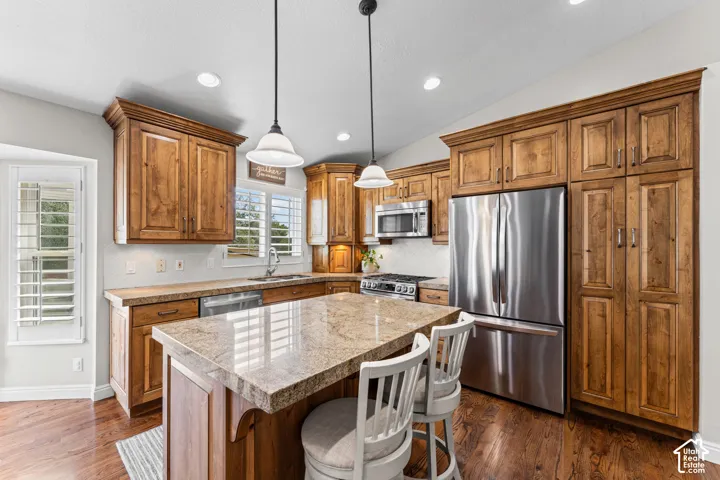 Kitchen featuring wood-finish cabinetry, stainless steel appliances, granite countertops, and a central island with pendant lighting