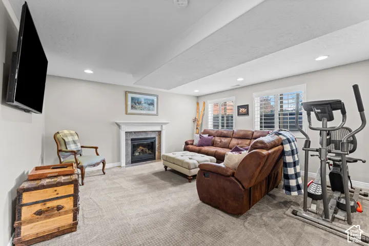 Recessed lighting, light gray wall color, carpeted flooring, fireplace with stone surround, and windows with white plantation shutters