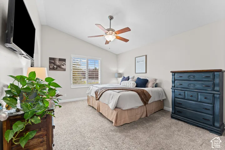 Vaulted ceiling with a ceiling fan, window with plantation shutters, and carpeted flooring