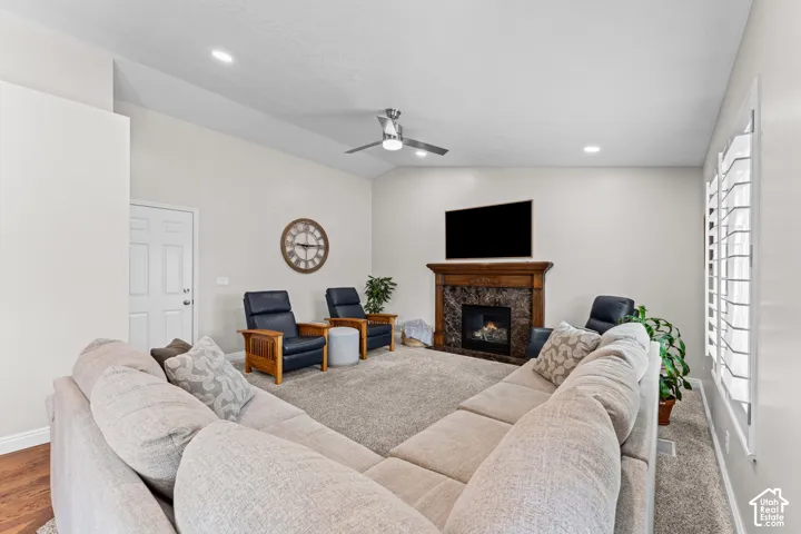 Spacious living area featuring a fireplace with a wood-finish mantel and stone surround, plantation shutters, recessed lighting, and a ceiling fan