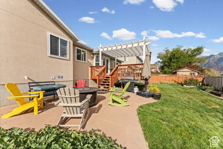 Expansive concrete patio with a fire pit, leading to a multi-level wooden deck with a white pergola