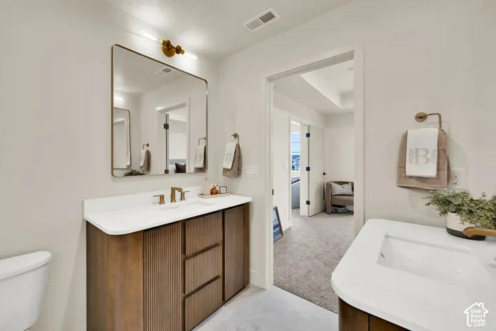 Dual wood-finish vanities with white countertops and integrated sinks, brushed brass fixtures, and a rectangular mirror with integrated lighting