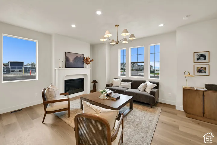 Recessed lighting, light wood-finish flooring, a decorative fireplace with a mantel, multiple windows, and a multi-arm chandelier