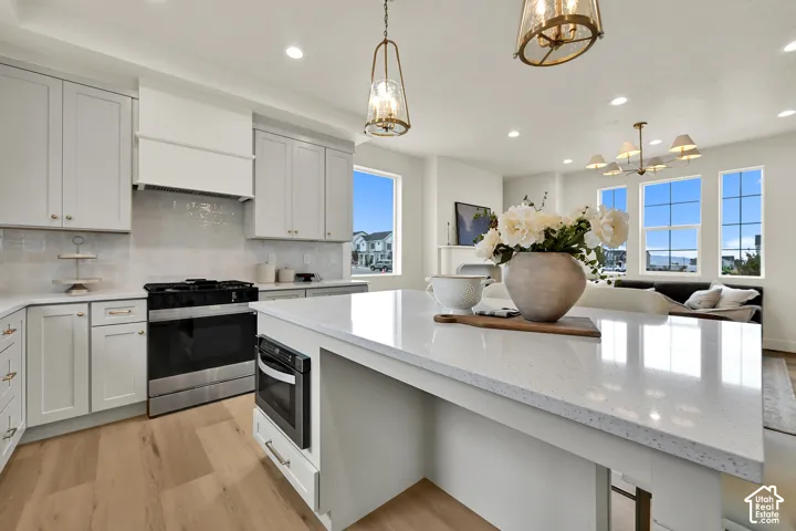 Light-toned perimeter cabinetry, a built-in microwave, wood-finish flooring, and a large central island with a solid surface countertop