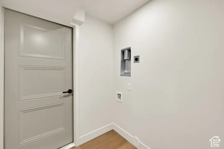 Light wood-finish flooring, white walls, and a gray panel door with a matte black handle