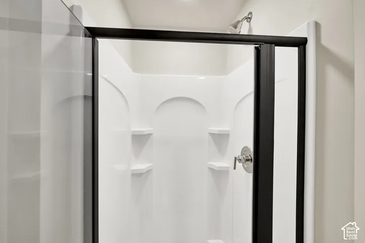 Enclosed shower with a white surround, built-in shelving, black-framed clear glass door, and a polished chrome shower head and fixtures