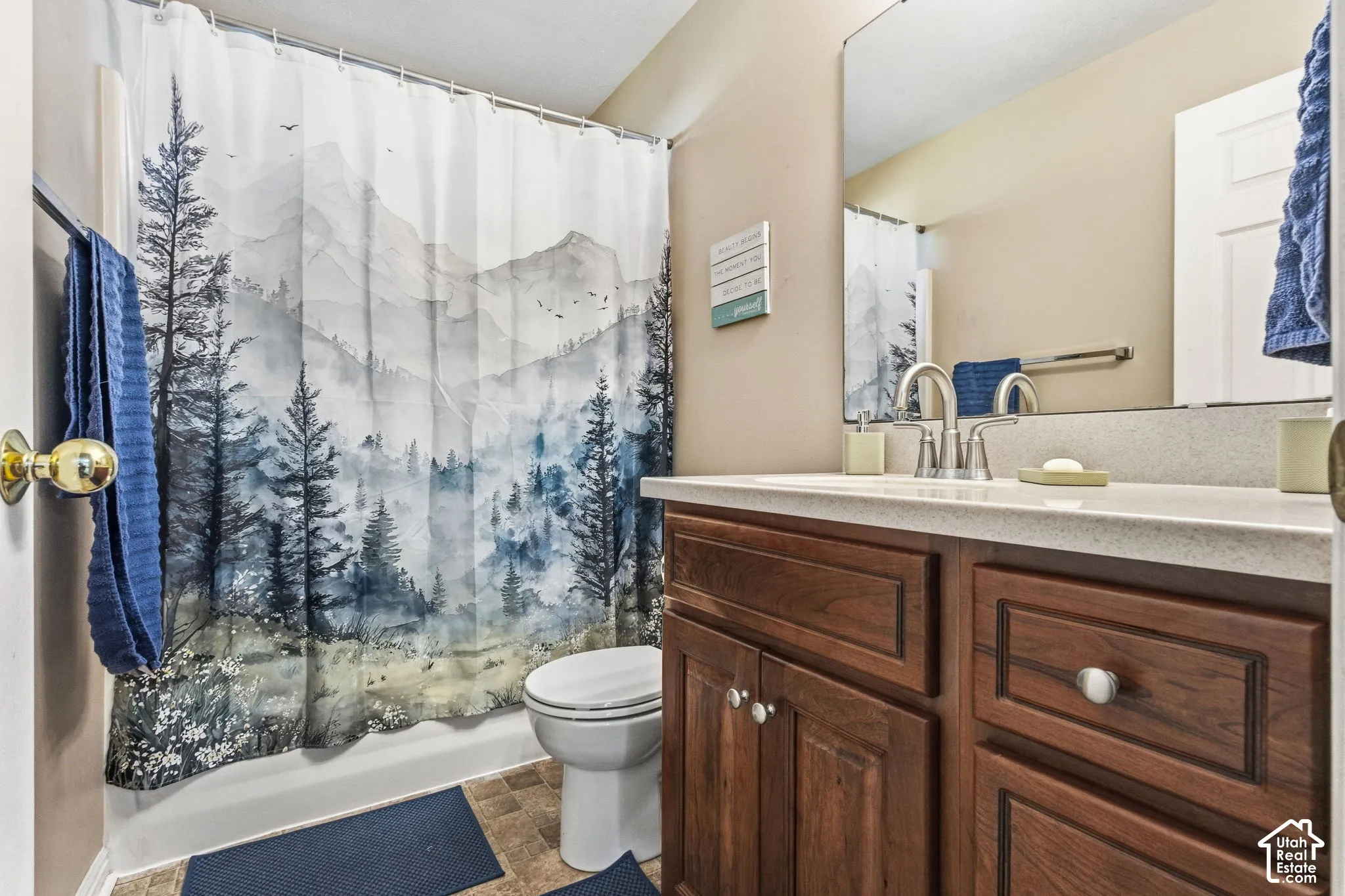 Vanity with wood-finish cabinetry, light-toned countertop, and undermount sink with chrome fixtures