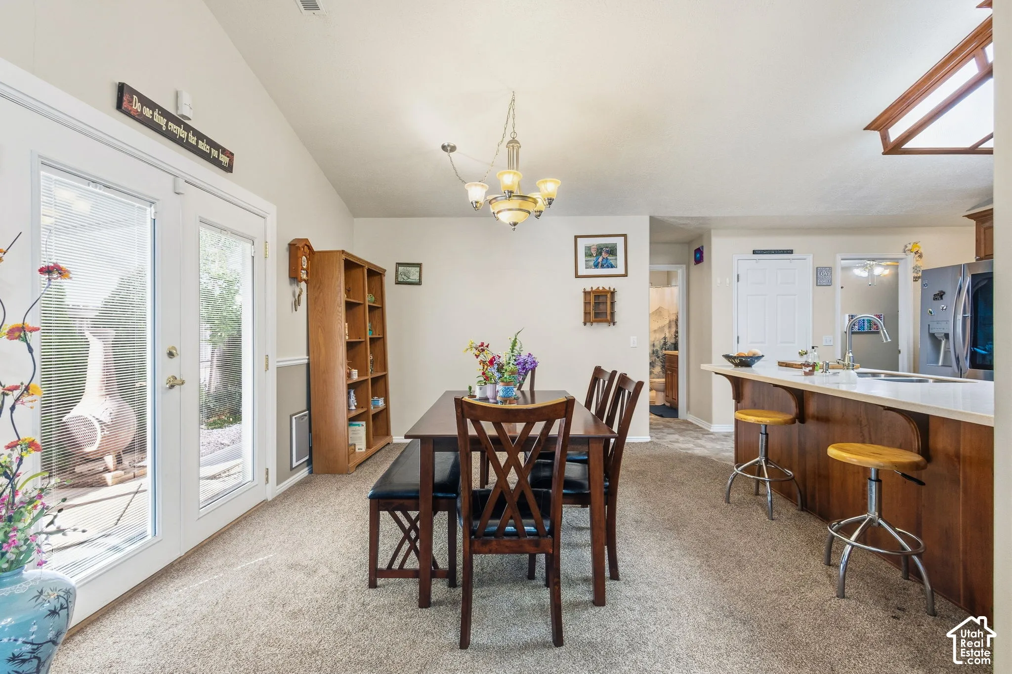 Vaulted ceiling, ceiling-mounted chandelier, glass-paneled double doors, breakfast bar with countertop, and wood-finish cabinetry