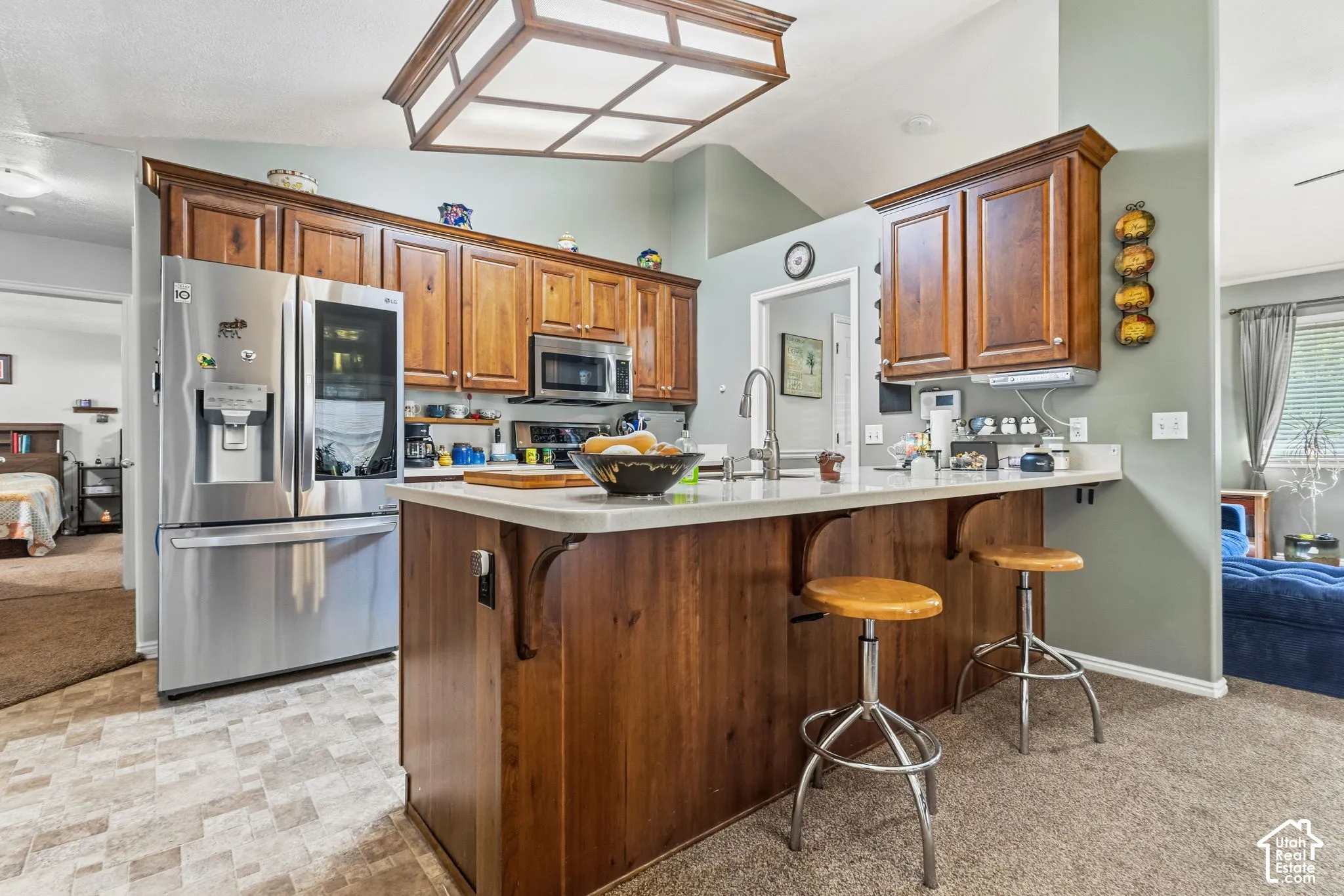 Kitchen featuring wood cabinetry, stainless steel appliances, a kitchen island with a light-toned countertop, and vaulted ceilings