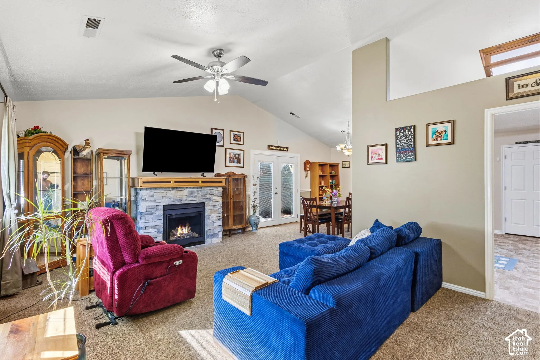 Vaulted ceiling with ceiling fan, stone-clad fireplace, and double French doors
