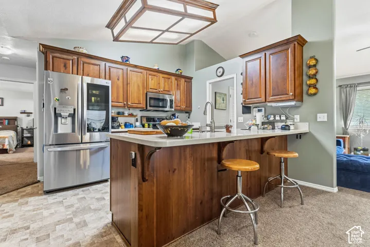Kitchen featuring wood cabinetry, stainless steel appliances, a kitchen island with a light-toned countertop, and vaulted ceilings