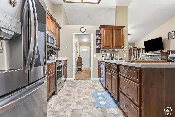 Kitchen featuring stainless steel appliances, wood cabinetry, light-toned countertops, and vaulted ceilings
