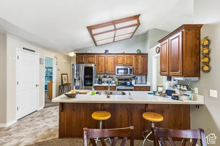 Kitchen with wood-finish cabinetry, stainless steel appliances, and a central island featuring a sink