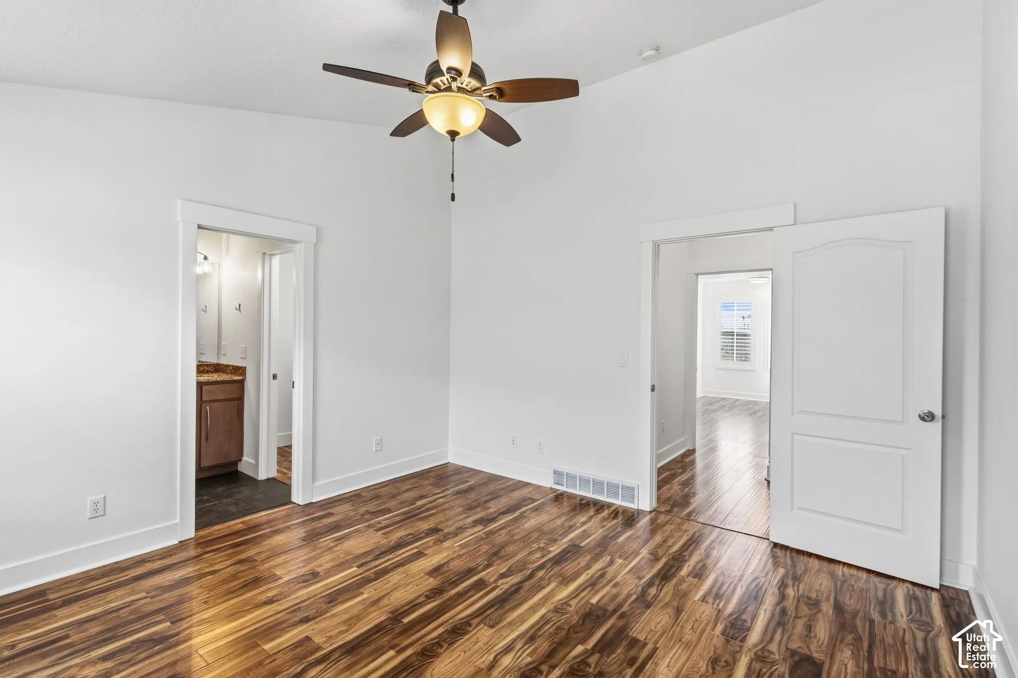 Wood-finish flooring, vaulted ceiling, ceiling fan with integrated lighting, white interior doors, and a vanity with a stone countertop