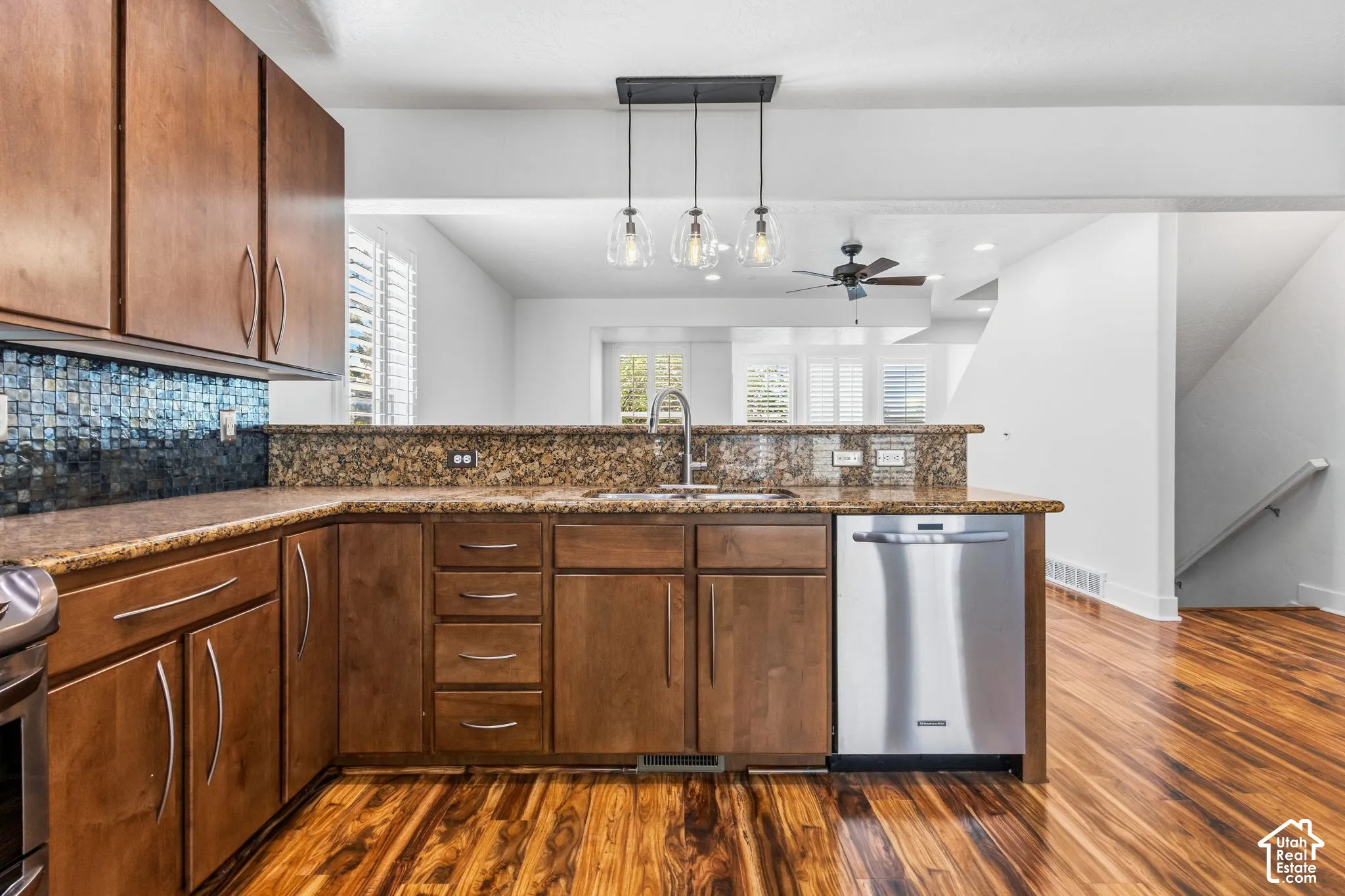 Kitchen featuring wood cabinetry, a mosaic tile backsplash, a stainless steel dishwasher, a kitchen island with seating, and a stainless steel sink with a gooseneck faucet