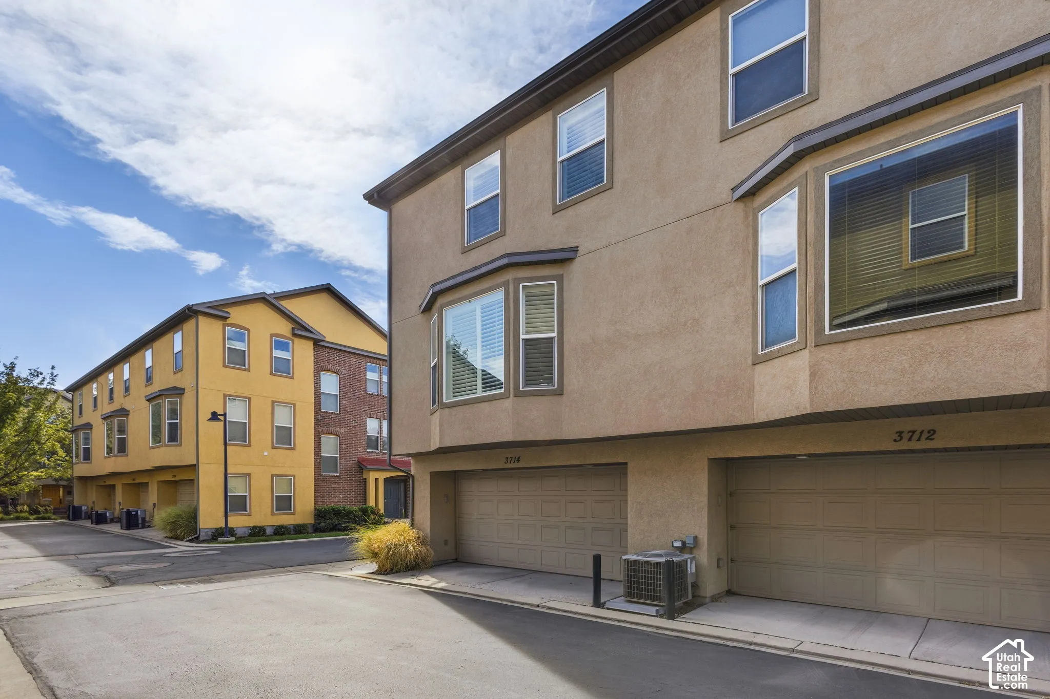 Stucco exterior with multiple bay windows, two integrated garage doors, and individual unit numbers