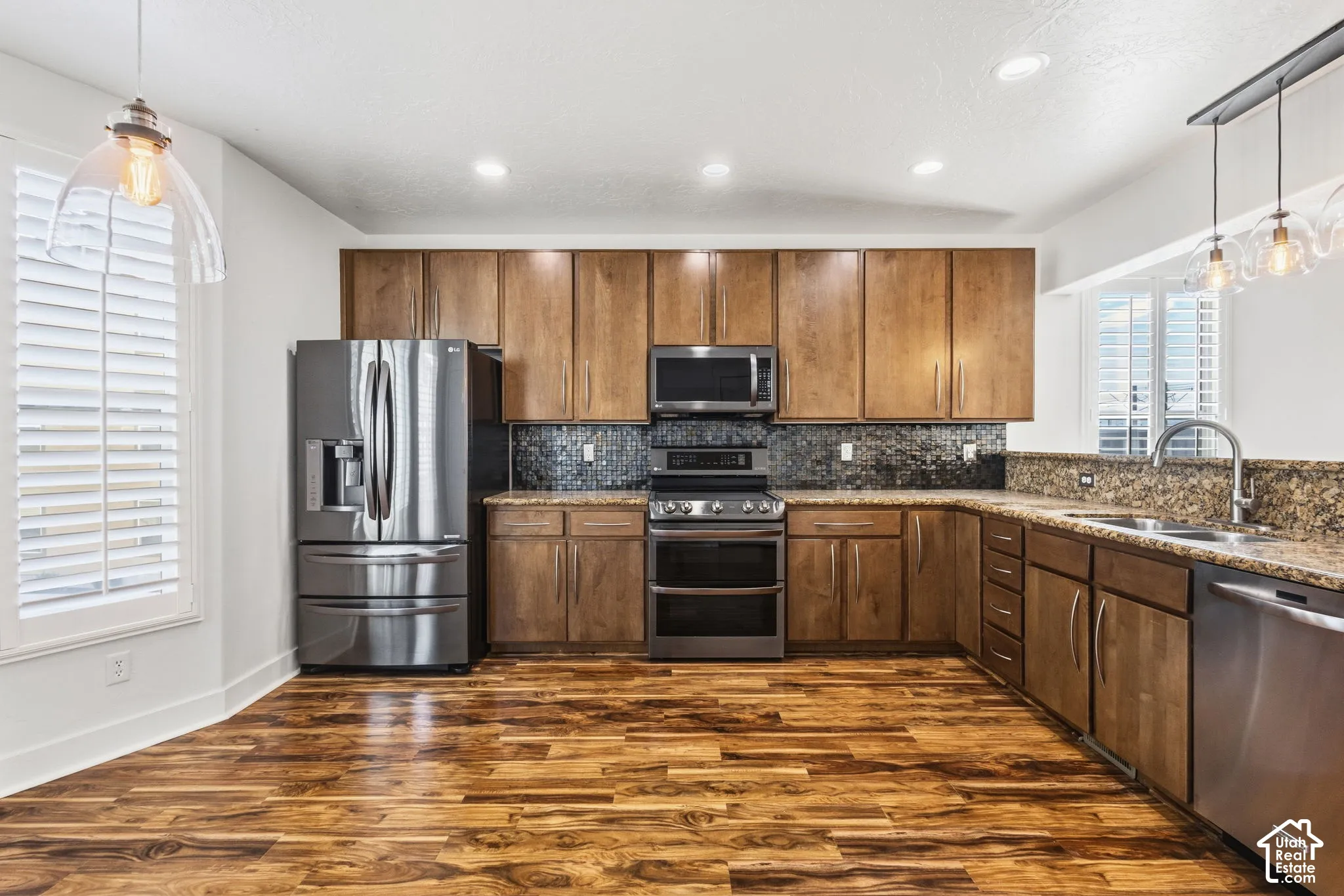 Kitchen featuring wood-finish flooring, stainless steel appliances, wood cabinetry, stone countertops, and a tiled backsplash