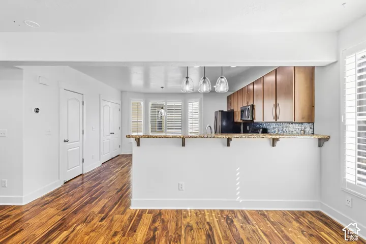 Wood-finish flooring, white walls, kitchen pass-through with granite countertop, wood cabinetry, and mosaic tile backsplash