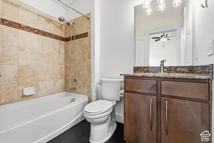 Bathroom featuring a vanity with a stone countertop, wood-finish cabinetry, a full-sized mirror, and a tub-shower combination with tiled surround and mosaic accent