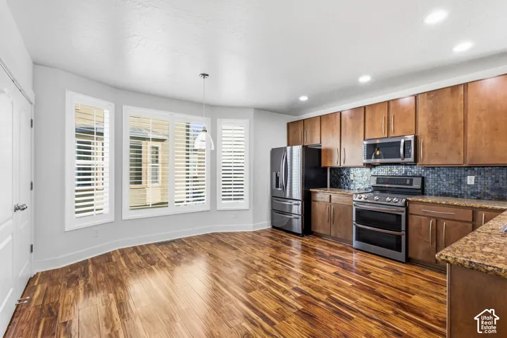 Recessed lighting, wood-finish flooring, stainless steel appliances, wood cabinetry, and a tile backsplash