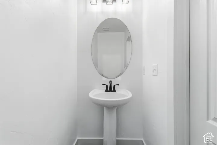 Pedestal sink with a black faucet, oval mirror, and a three-light vanity fixture