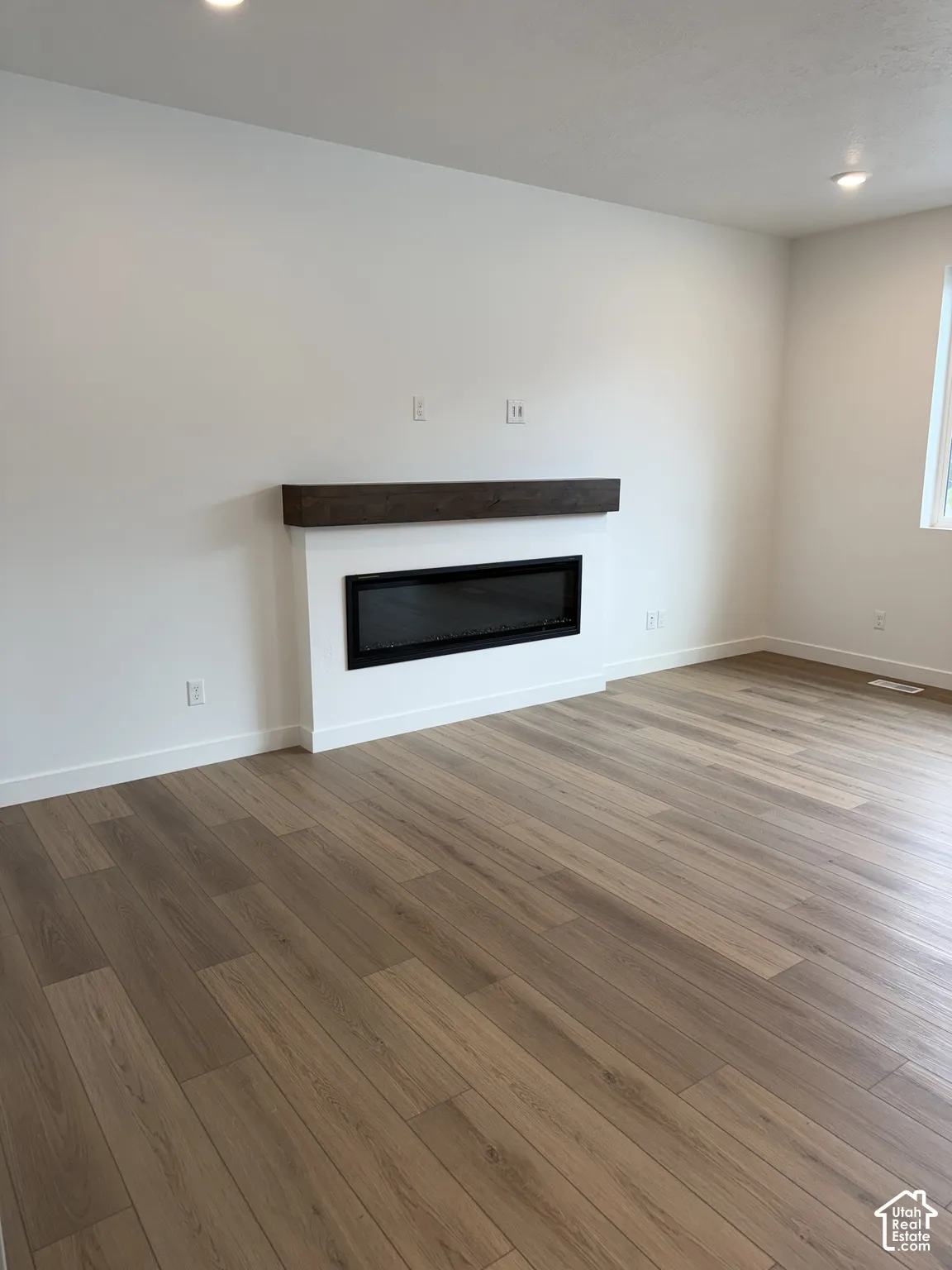 Wood-finish flooring, recessed lighting, and a modern linear fireplace with a wood mantel