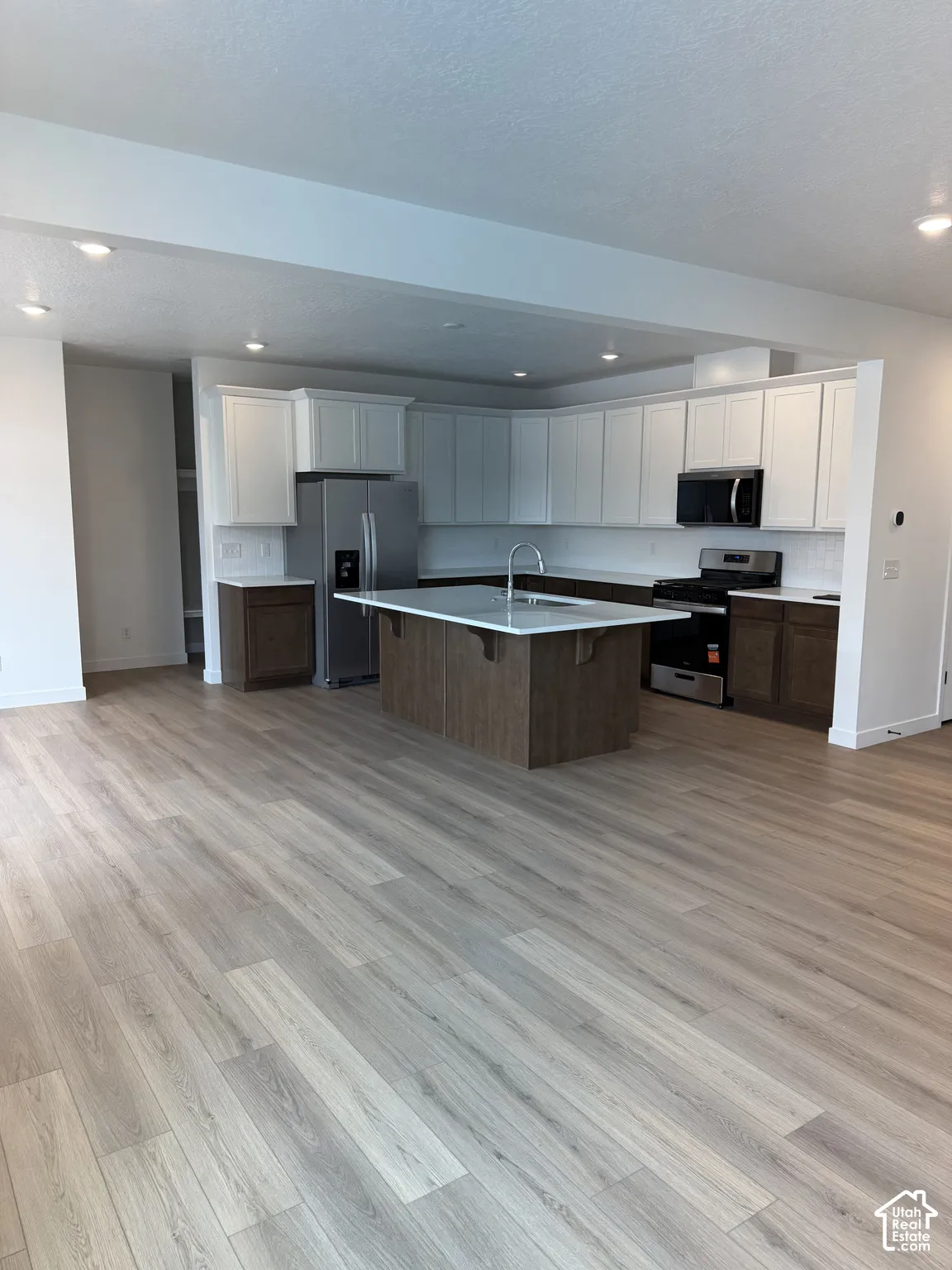 Contemporary kitchen featuring white upper cabinetry, dark wood-finish lower cabinetry, a center island with a sink, and stainless steel appliances