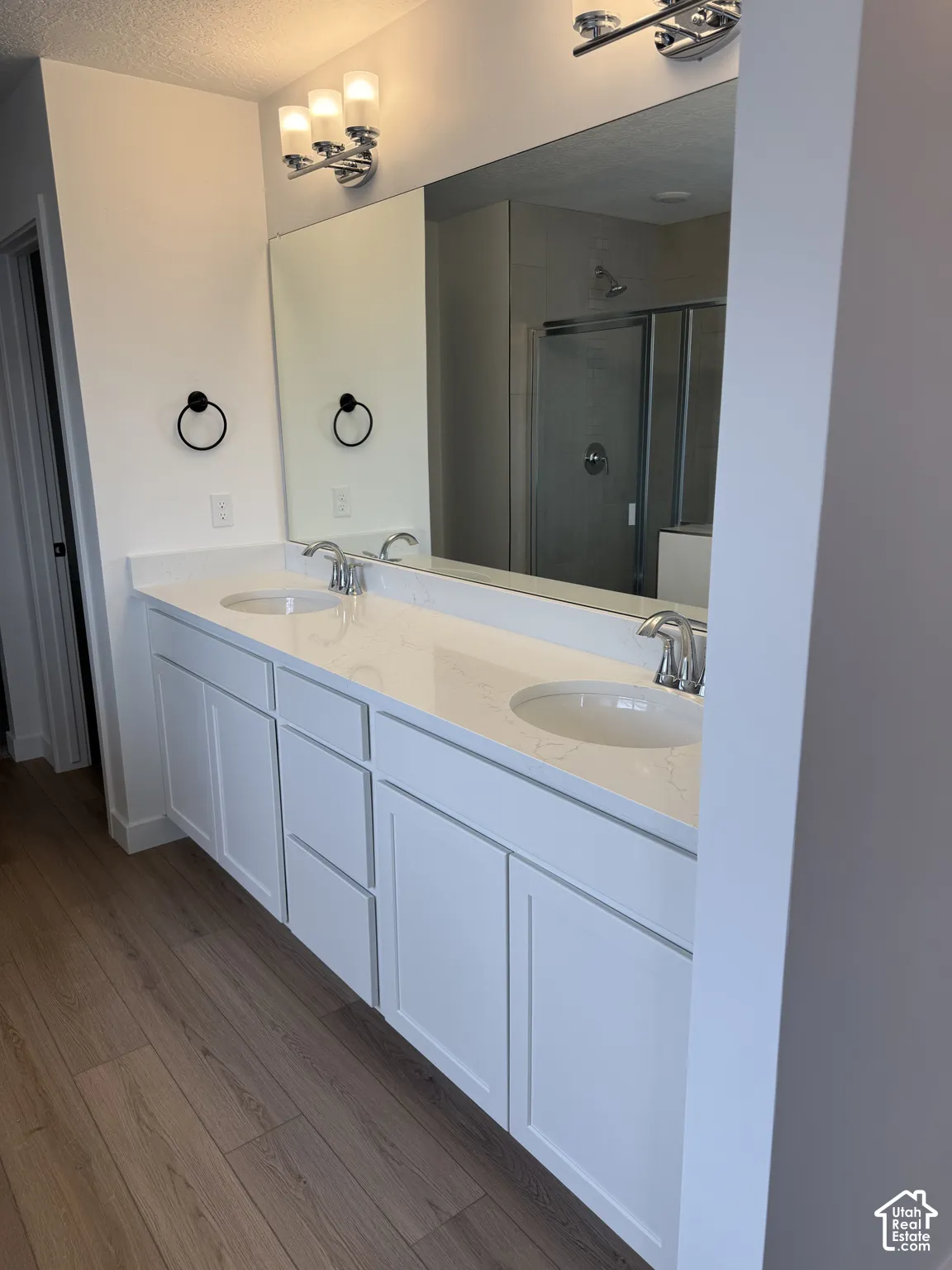 Dual vanity with white cabinetry, light-toned countertop, chrome fixtures, and wood-finish flooring