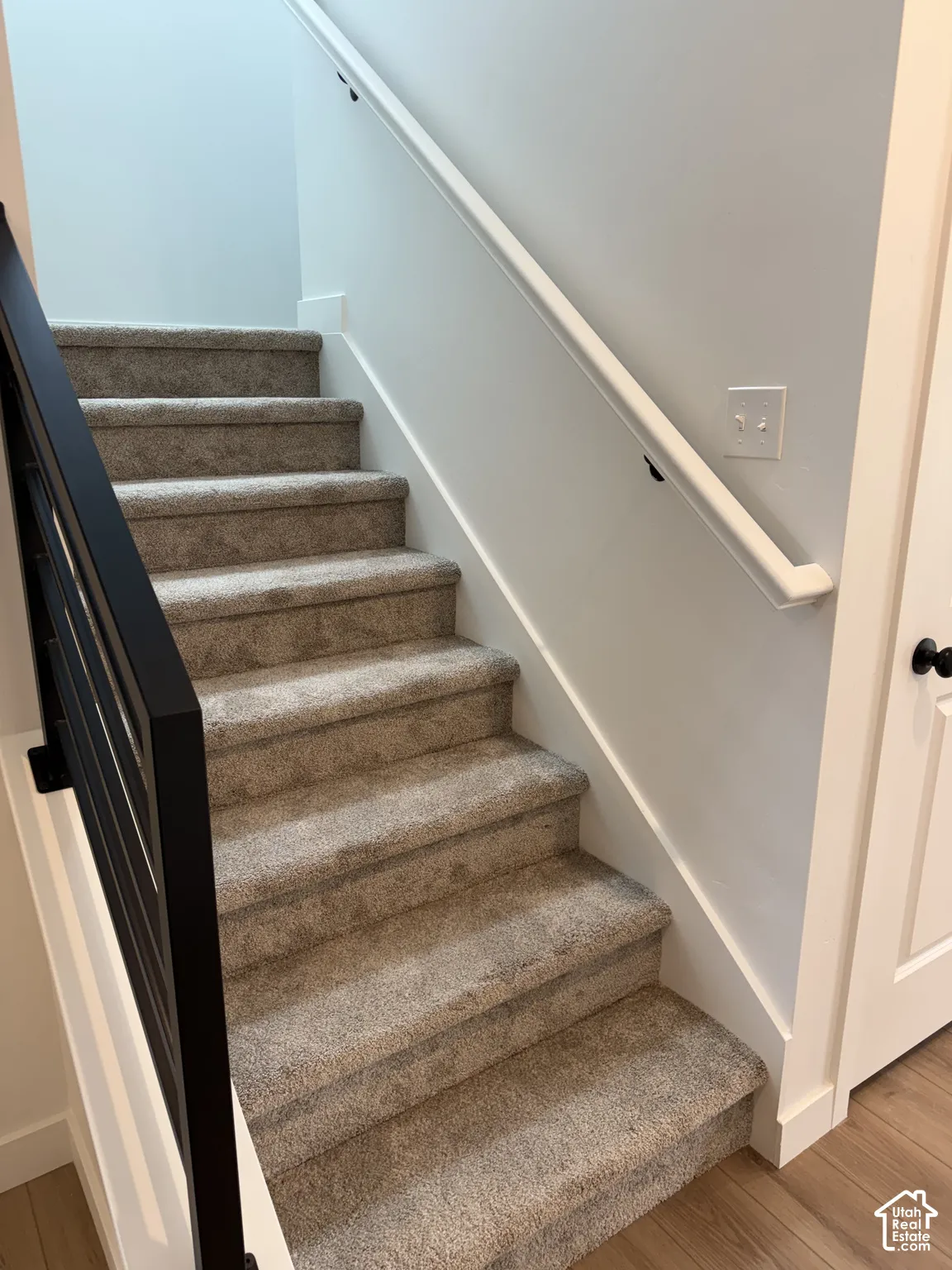 Carpeted staircase with a modern black iron railing and a white wall-mounted handrail