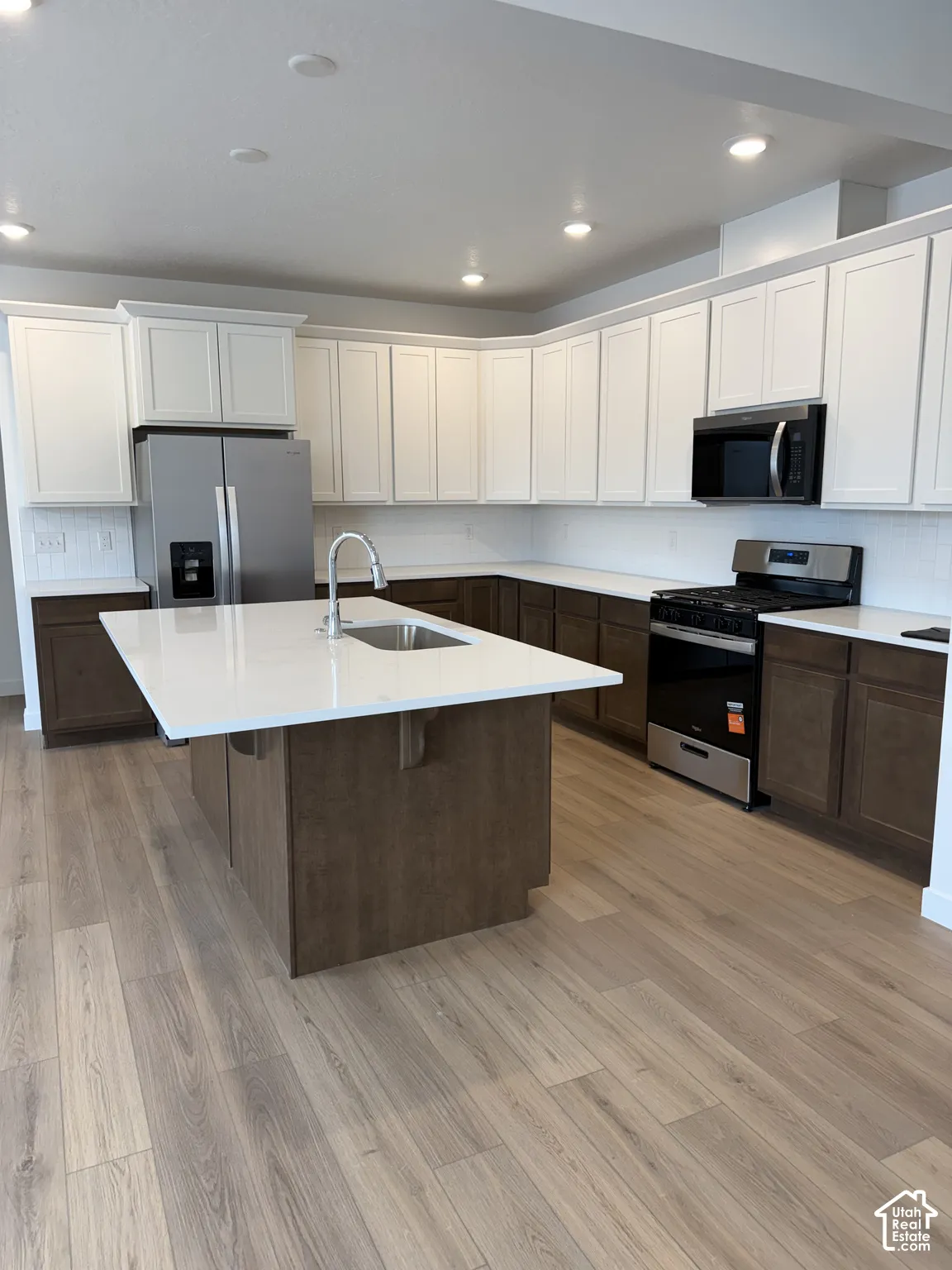 Kitchen featuring a central island with an undermount sink, stainless steel appliances, two-tone cabinetry, and wood-finish flooring
